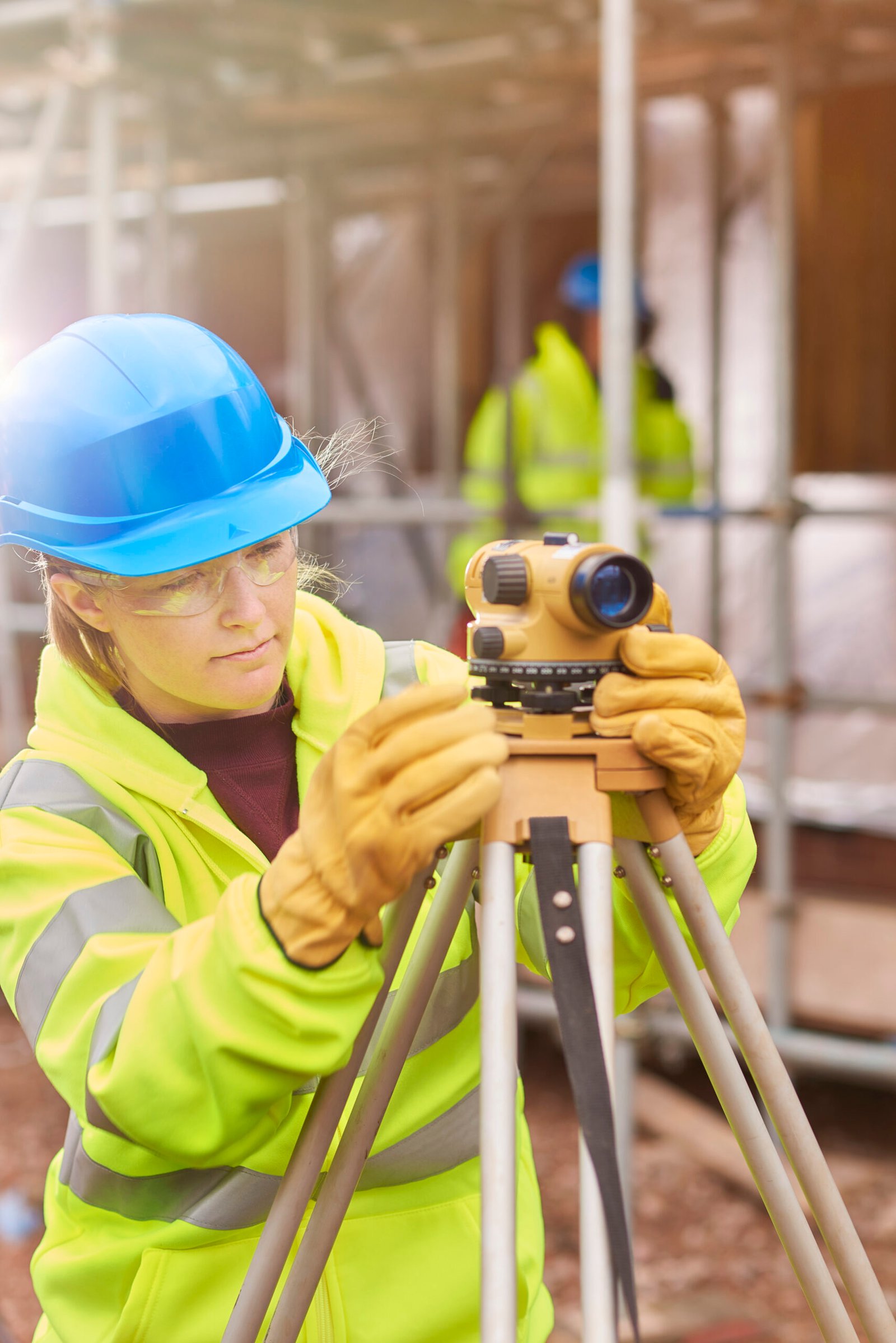 a female construction worker stands behind a builder's level on a building site .She is smiling proudly to camera.